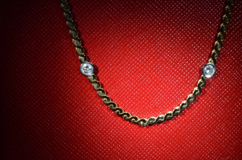 May include: A gold chain necklace with two small, clear gemstones. The necklace is on a red background.