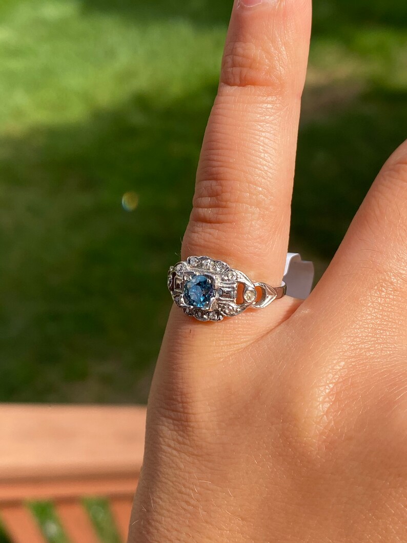 K&ouml;nnte beinhalten: Ein silberner Ring mit einem blauen Edelstein, der von kleineren, klaren Edelsteinen umgeben ist.