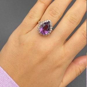 May include: A pear-shaped amethyst ring with a halo of smaller diamonds set in a white gold band.