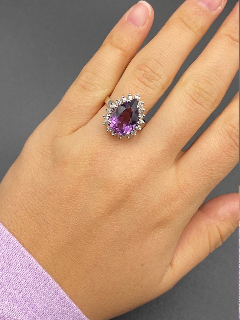 May include: A pear-shaped amethyst ring with a halo of smaller diamonds set in a white gold band.