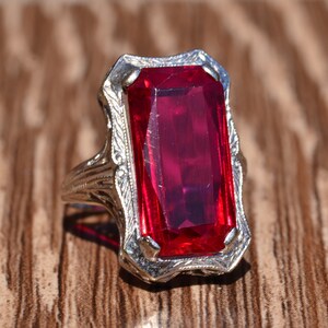 May include: A vintage ring featuring a large, rectangular, red gemstone set in a filigree design.