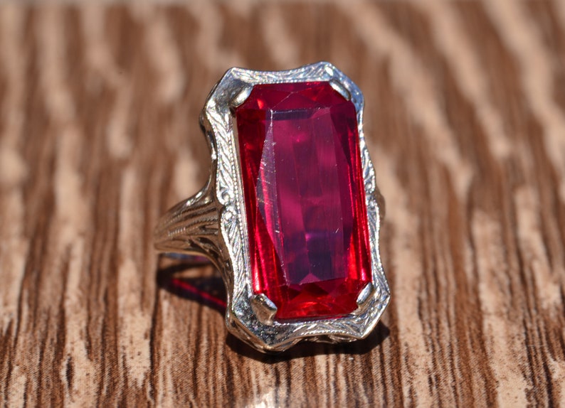 May include: A vintage ring featuring a large, rectangular, red gemstone set in a filigree design.
