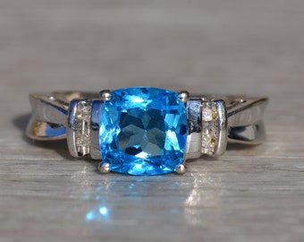 May include: A silver ring with a large, cushion-cut blue topaz gemstone and two smaller accent diamonds.
