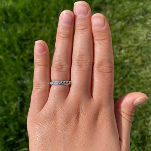 May include: A silver band ring with small, clear gemstones set in a pave setting.