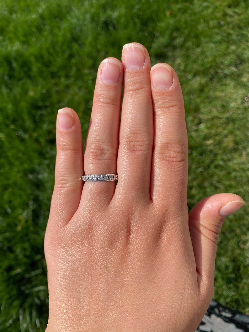 May include: A silver band ring with small, clear gemstones set in a pave setting.