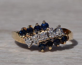May include: A gold ring with a cluster of blue sapphires and white diamonds set in a wave-like design.
