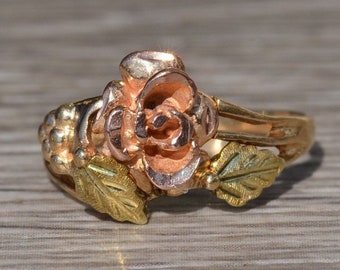 May include: A gold and rose gold ring with a rose design. The rose is made of rose gold and the leaves are made of green gold.