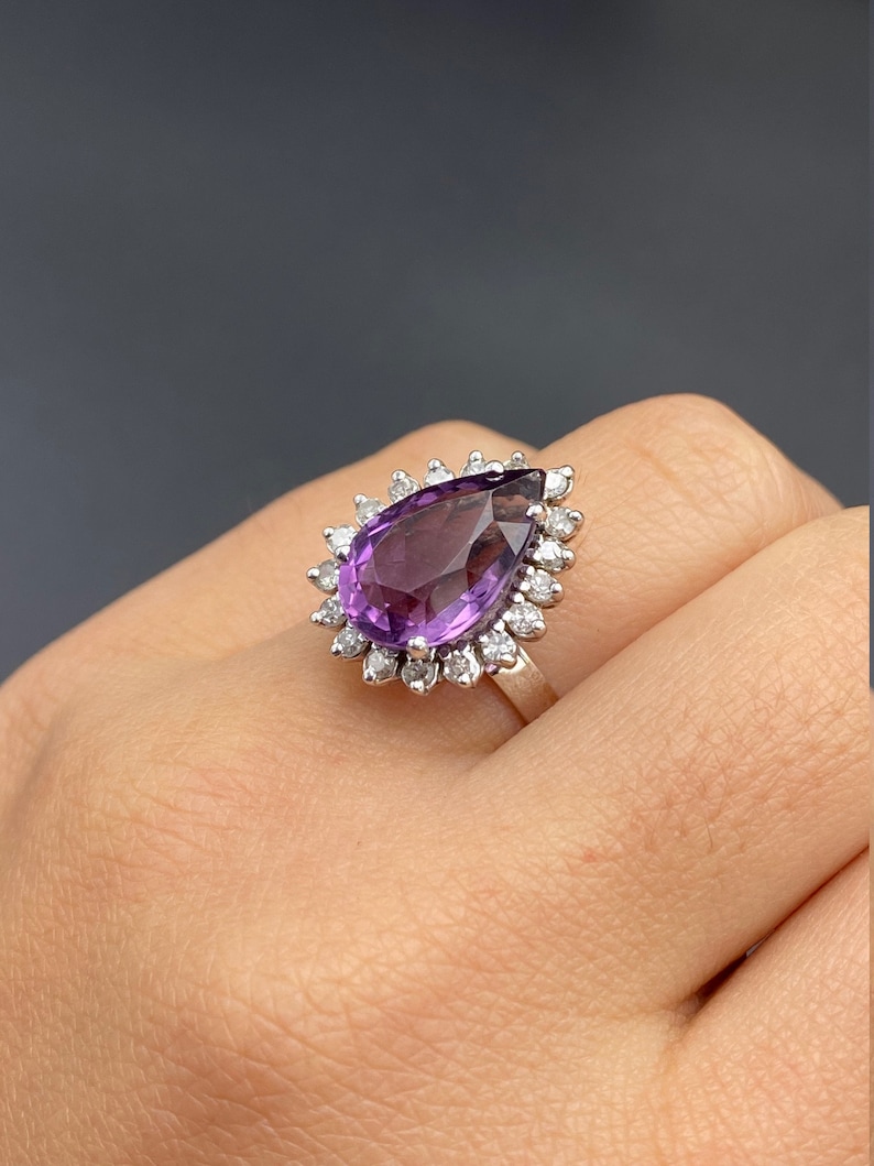May include: A pear-shaped amethyst ring with a halo of small diamonds set in silver.