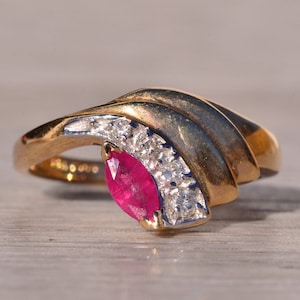 May include: A gold ring featuring a pink ruby and small diamonds set in a curved design.