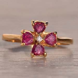 Könnte beinhalten: Ein goldener Ring mit einem Blumendesign, das vier rosafarbene herzförmige Steine und einen einzelnen weißen Diamanten in der Mitte zeigt.