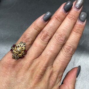 May include: A gold ring with a floral design set with small red and white stones.