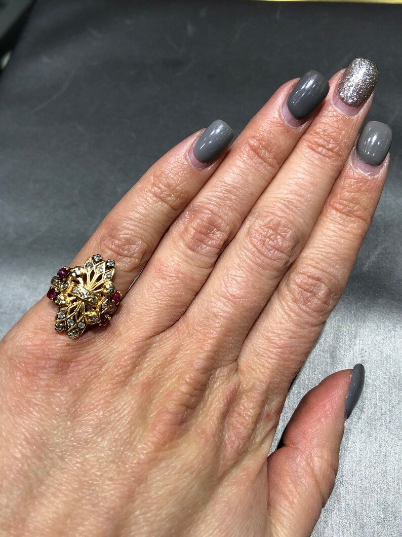 May include: A gold ring with a floral design set with small red and white stones.