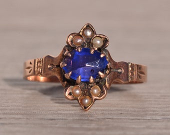May include: A vintage ring with a blue sapphire gemstone surrounded by small pearls. The ring is made of gold and has a delicate design.