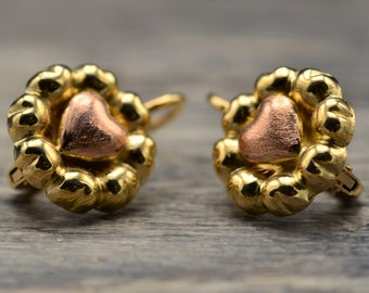 Puede incluir: Un par de pendientes de oro con un diseño en forma de corazón. Los corazones son de dos tonos, con un borde exterior dorado y un centro de oro rosa.