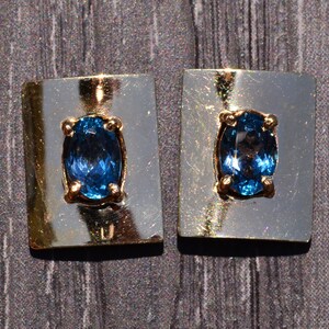 Puede incluir: Un par de pendientes con una piedra ovalada azul engastada en un engaste de oro y plata.