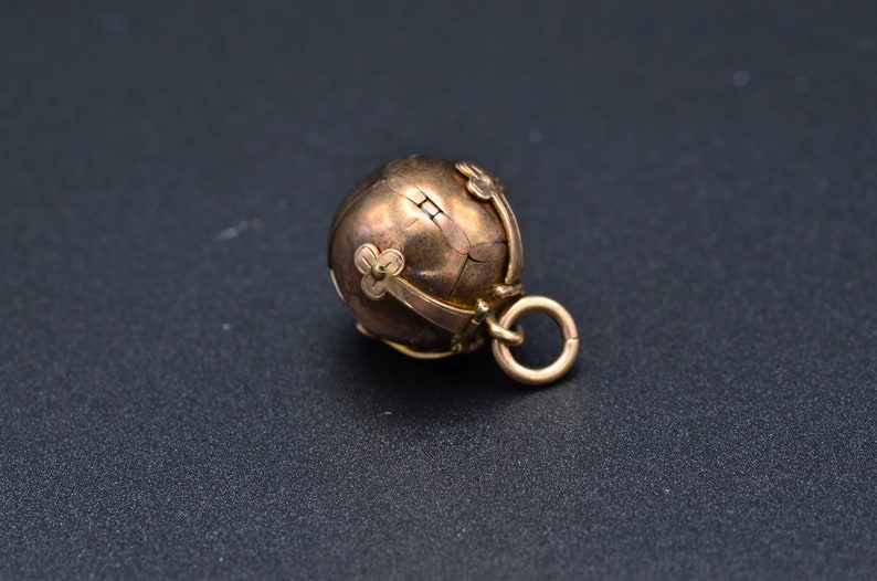 May include: A gold-toned metal charm in the shape of a sphere with a decorative design. The sphere is decorated with small, raised flower-like shapes and has a loop at the top for attaching to a chain or bracelet.