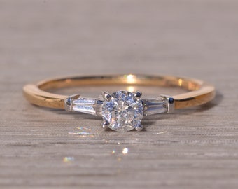 May include: A gold and white engagement ring with a round center diamond and two baguette diamonds on either side.