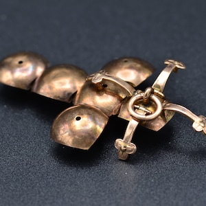 May include: A gold-toned metal pendant with a cross-shaped design. The pendant is made up of five round, dome-shaped pieces connected by a hinge. The pendant has a small loop at the top for attaching a chain.