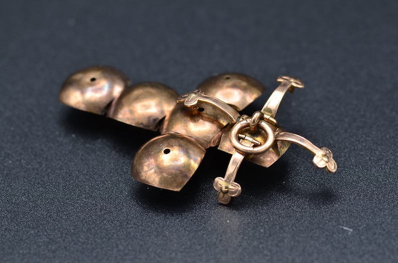 May include: A gold-toned metal pendant with a cross-shaped design. The pendant is made up of five round, dome-shaped pieces connected by a hinge. The pendant has a small loop at the top for attaching a chain.