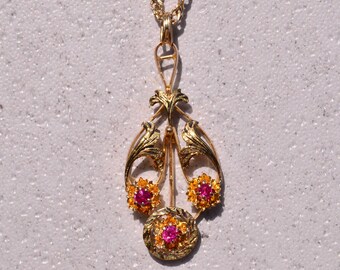 May include: A gold pendant necklace with a delicate, ornate design featuring three pink and yellow flower accents.