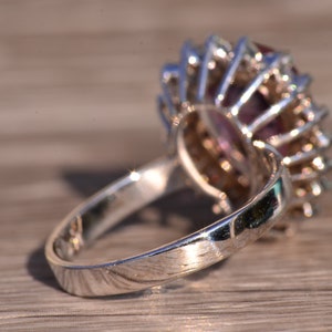 May include: A silver ring featuring a large, faceted purple gemstone encircled by smaller clear gemstones.