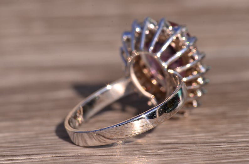 May include: A silver ring featuring a large, faceted purple gemstone encircled by smaller clear gemstones.