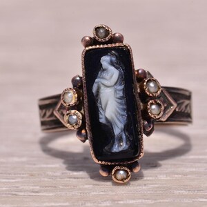 Pu&ograve; includere: Anello antico con cammeo nero rettangolare raffigurante una figura classica bianca. L'anello ha una montatura color oro con piccole perle e accenti decorativi. La fascia ha un design inciso.