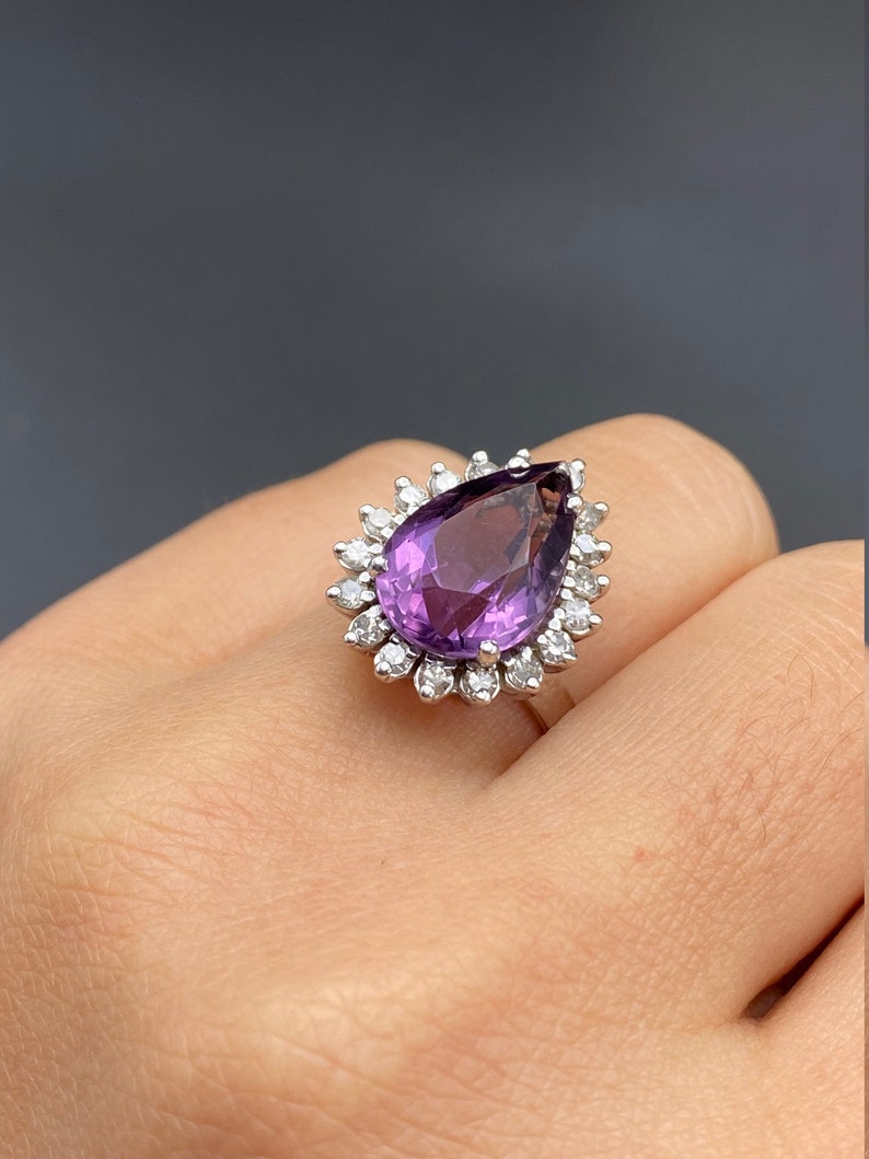 May include: A pear-shaped amethyst ring with a halo of smaller diamonds set in silver.