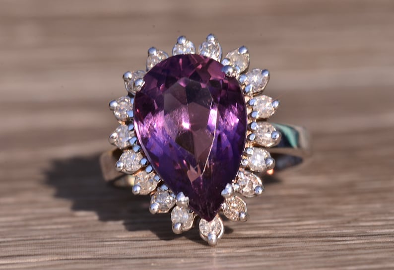 May include: A pear-shaped amethyst ring with a halo of smaller diamonds set in silver.
