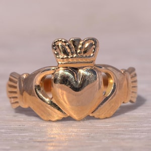 May include: A gold-toned Claddagh ring with a heart, hands, and crown design.