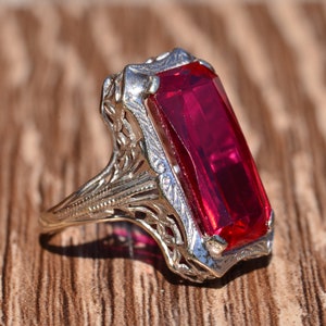 May include: A vintage ring featuring a large, rectangular, red gemstone set in a filigree design.