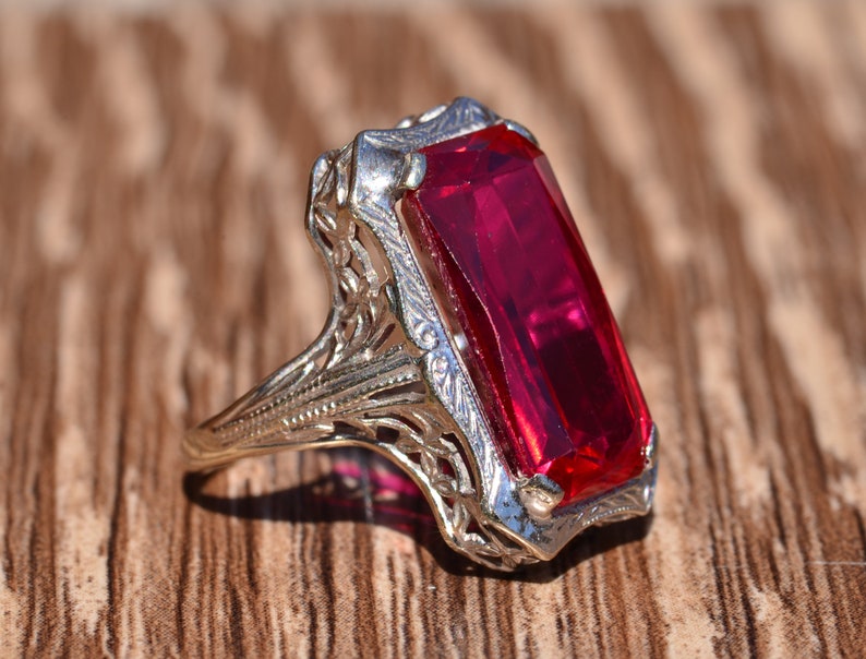 May include: A vintage ring featuring a large, rectangular, red gemstone set in a filigree design.