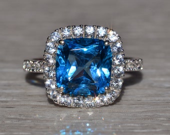 May include: A silver ring with a large, square-shaped blue topaz gemstone surrounded by a halo of smaller, clear diamonds.