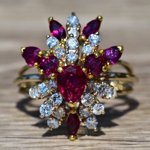 Puede incluir: Un anillo de oro con un gran rubí en forma de pera rodeado de rubíes y diamantes más pequeños.