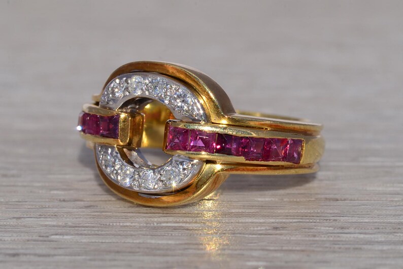 May include: A gold ring with a distinctive design. The ring has a central, circular feature with a band of small, square-cut rubies and a band of small diamonds. The ring's band is also gold.