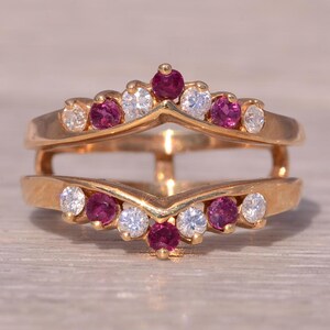 Pode incluir: Um anel de ouro com um design em forma de V, com uma fileira de pedras de rubi e diamantes alternadas.