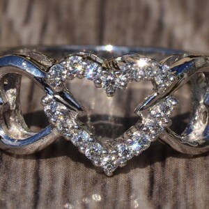 May include: A silver ring with two intertwined hearts, one of which is outlined with small sparkling diamonds.