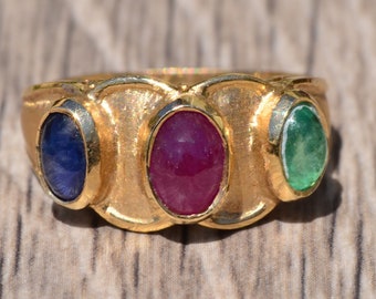 May include: A gold ring set with three oval-shaped gemstones. The gemstones are a blue sapphire, a red ruby, and a green emerald.