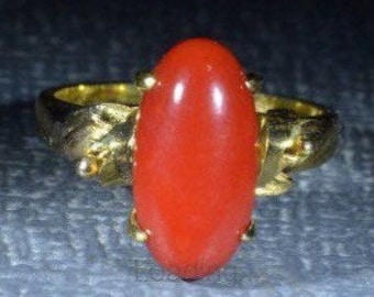 May include: A red oval gemstone ring set in a gold band with a twisted design.