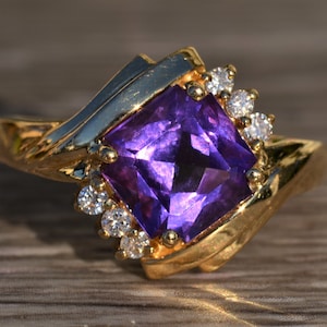 May include: A gold ring with a large, square-shaped amethyst gemstone surrounded by smaller diamonds.