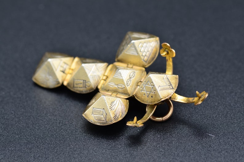 May include: A gold-colored pendant with a hinged, multi-sided design. Each side features a different engraved symbol, including a Star of David, a pyramid, and a menorah.