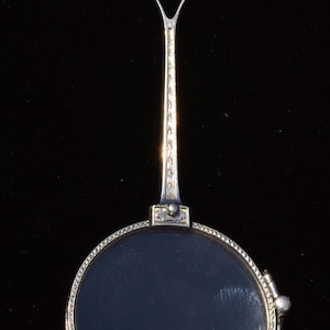 Puede incluir: Un colgante de lupa de plata con una cadena y una lente redonda. El colgante está diseñado con un patrón geométrico decorativo.