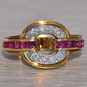 May include: A gold ring with a distinctive design, featuring a central open circle. The ring is embellished with sparkling white diamonds and vibrant red gemstones. The gemstones are set in a channel setting, enhancing the ring's elegance.