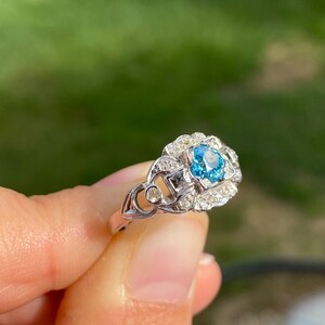 K&ouml;nnte beinhalten: Ein silberner Ring mit einem blauen Edelstein, der von kleineren wei&szlig;en Edelsteinen umgeben ist.