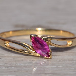 May include: A gold ring with a pink marquise-shaped gemstone set in a delicate, twisted band.