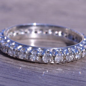 May include: A silver band ring with a row of small, clear diamonds set in a continuous line around the band.