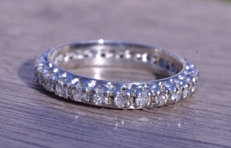 May include: A silver band ring with a row of small, clear diamonds set in a continuous line around the band.