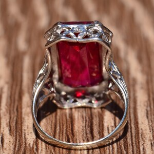 May include: A silver ring featuring an emerald-cut red gemstone set in a filigree design.