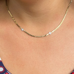 May include: A gold chain necklace with two small clear stones. The chain is a delicate, wavy design.