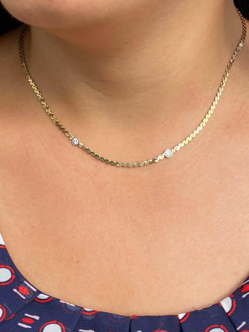 May include: A gold chain necklace with two small clear stones. The chain is a delicate, wavy design.